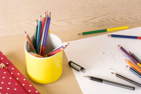 Yellow cup on the wood texture with toy and red notebook, white paper, penの写真素材