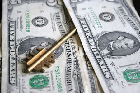 paper dollar bills and metallic key resting upon dark backgroundの写真素材