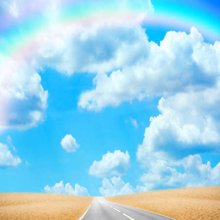 road in desert under sky with rainbowの写真素材