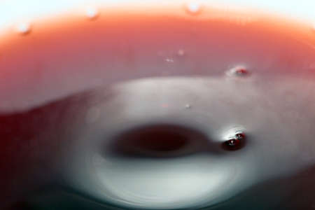 Ripples on the surface of a dark red liquid in a container after its pouringの写真素材