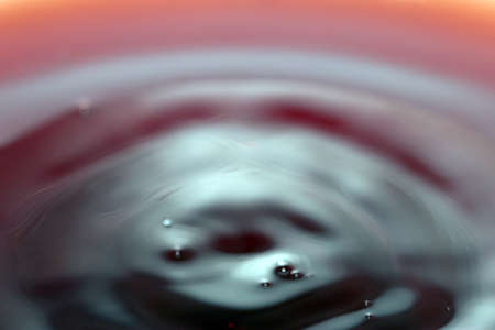 Ripples on the surface of a dark red liquid in a container after its pouringの写真素材