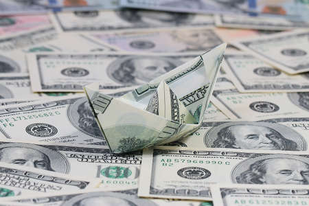 a ship folded from a paper bill American dollars on a pile of moneyの写真素材