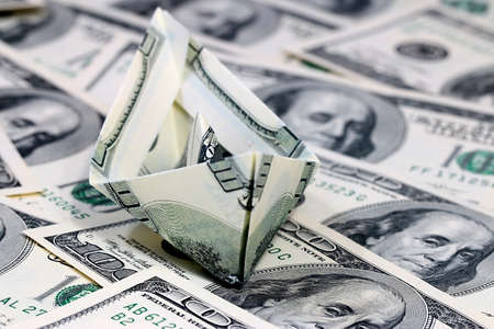 a ship folded from a paper bill American dollars on a pile of moneyの写真素材