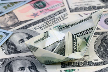 a ship folded from a paper bill American dollars on a pile of moneyの写真素材