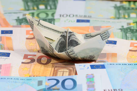 a boat built of American hundred dollar bills standing on a pile of paper euros, origamiの写真素材