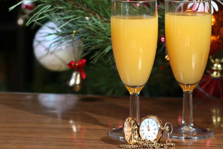 New Year decorations on the Christmas tree, two glasses of juice and an antique clock in a gold caseの写真素材