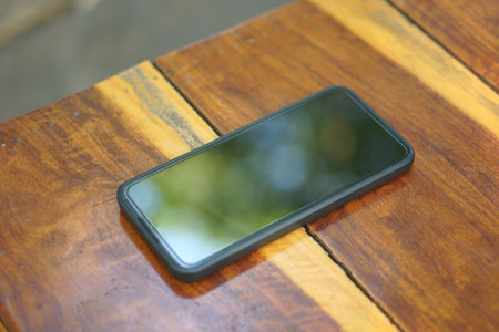 A black phone is placed on a brown wooden floor.の写真素材