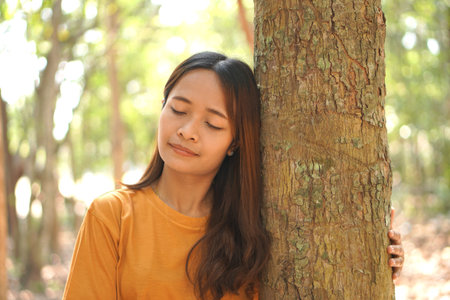 concept of saving the world Asian woman holding a tree with her eyes closed to experience the power of natureの写真素材