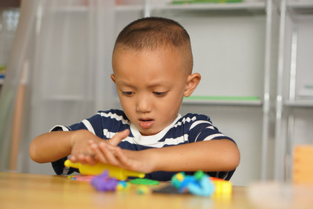 Boy making plasticine to promote development on the table in the house. Plasticine comes in many...