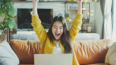 Beautiful Asian girl celebrate with laptop, success happy pose. E-commerce, university education, internet technology, or startup small business concept. Modern office or living room with copy spaceの素材