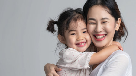 cheerful asian toddler daughter hugging happy mother isolated on grayの素材