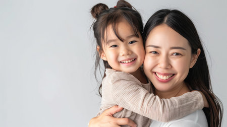 cheerful asian toddler daughter hugging happy mother isolated on grayの素材