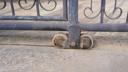 This close-up image showcases a rusty gate wheel mechanism resting on a concrete path, highlighting the details of aging metal and functional design in outdoor settings.の写真素材