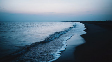 A calm ocean with soft, gentle waves rolling towards a quiet, empty beach at dusk.の素材
