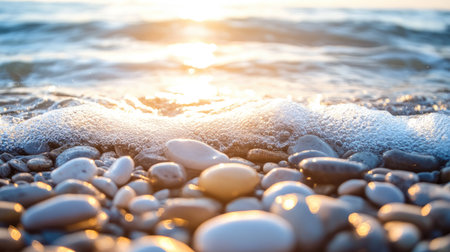 A smooth pebble beach with sunlit stones gently rounded by waves, water softly washing over themの素材