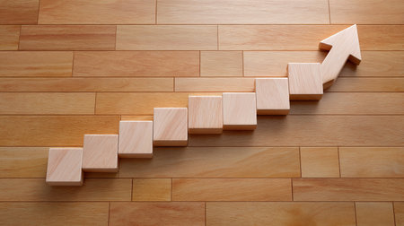 A visually appealing arrangement of wooden blocks forming an upward growth arrow on a hardwood floor, symbolizing progress and success in business and development.の素材