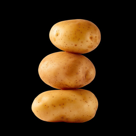 A stunning image of three fresh potatoes stacked elegantly against a black background, showcasing their rustic beauty and natural texture, ideal for food photography.の素材
