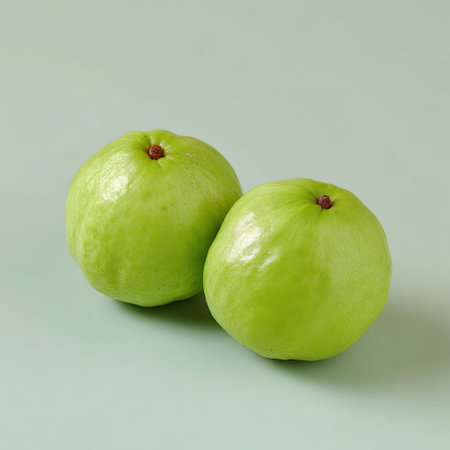 Two ripe green guavas sit on a soft pastel surface, showcasing their smooth texture and vibrant color. Ideal for health and culinary themes.の素材