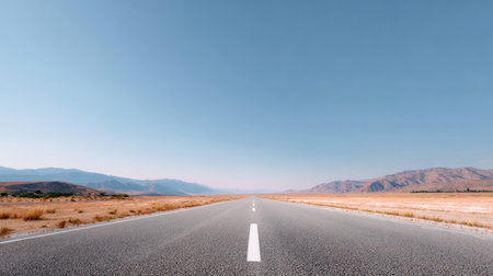 A breathtaking view of a long, empty road stretching through a vast desert landscape. The clear blue sky and mountains in the background create a serene and tranquil atmosphere, inviting exploration and adventure.の素材