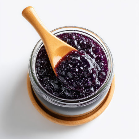 A close-up view of rich blueberry jam in a clear glass jar, accompanied by a wooden spoon, showcasing the glossy texture and vibrant color.の素材