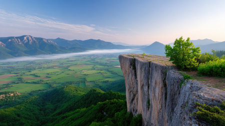 An awe-inspiring view from a high cliff, showcasing a vibrant green valley below with mountains in the distance, bathed in warm morning light.の素材