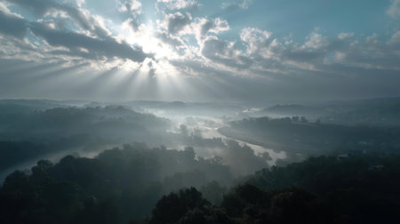 A stunning landscape captures the beauty of a misty river at dawn, illuminated by rays of sunlight breaking through clouds, creating a serene and tranquil atmosphere.の素材