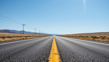 A vast open road stretches into the horizon under a clear blue sky. Power lines run alongside, highlighting a sense of freedom and solitude. Ideal for travel-themed projects.の素材