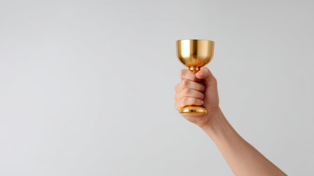 A hand proudly holds gleaming golden trophy, symbolizing achievement and success. minimalist background emphasizes trophy shine and emotion of victoryの素材