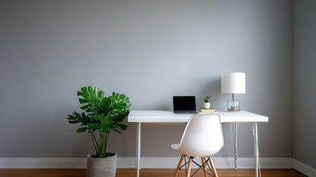 A clean workspace featuring white desk, laptop, small plant, and lamp against neutral gray wall creates calming and productive environmentの素材