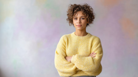A teenage girl with curly hair stands confidently with her arms crossed, wearing cozy yellow sweater. soft, pastel background adds warm and inviting atmosphere to portraitの素材