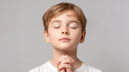 A serene image of a young boy with closed eyes and clasped hands in a thoughtful pose, capturing innocence and spirituality in a calming, neutral setting.の素材