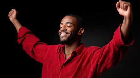 A joyful man celebrating with raised arms, wearing red shirt, smiling brightly against dark background. his expression conveys happiness and freedom, embodying moment of pure joyの素材