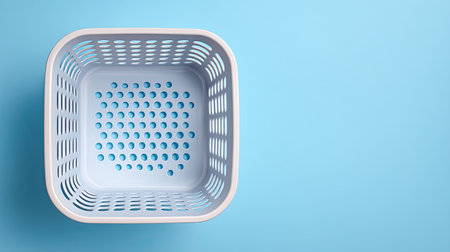 A top view of empty shopping basket on light blue background, showcasing its perforated design and clean lines, evokes sense of simplicity and organizationの素材