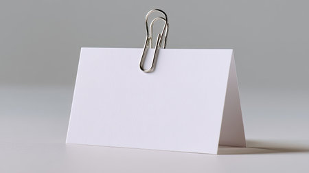 A minimalist blank card secured with a silver paper clip sits on a soft gray surface, ideal for presentations, note-taking, or creative projects. Perfect for showcasing messages or for use in office settings.の素材