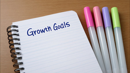 A neatly arranged notebook featuring the phrase "Growth Goals" alongside colorful markers on a wooden table, symbolizing motivation and planning for success.の素材