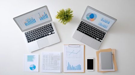 A modern workspace setup featuring two laptops with various charts and documents, accompanied by a smartphone and stationery, ideal for business analysis.の素材