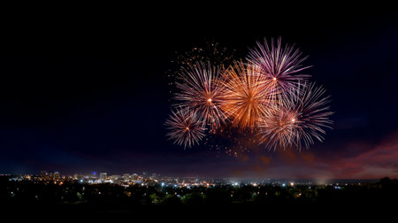 A fireworks exploding above distant city lights create vibrant celebration in night sky, illuminating urban landscape with colorful bursts of light and joyの素材