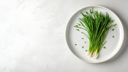A vibrant bunch of fresh chives displayed on a simple white plate, perfect for adding flavor and a garnish to various dishes in a healthy meal.の素材