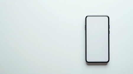 A sleek smartphone lies on a clean white surface with a blank screen, perfect for showcasing designs, app interfaces, and minimalistic technology presentations.の素材