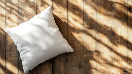 A soft white pillow rests on a warm wooden floor, illuminated by natural light creating beautiful shadow patterns, evoking a sense of calm and cozy atmosphere.の素材