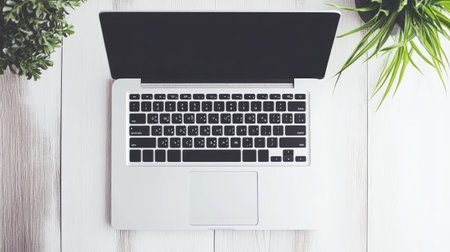 A top view of a sleek laptop on a wooden table, surrounded by vibrant green plants, perfect for creating an inspiring and productive workspace atmosphere.の素材