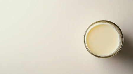 A glass filled with creamy milk sits elegantly on a light beige surface, symbolizing freshness and the wholesome nature of dairy in daily nutrition.の素材