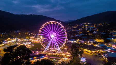 Experience the vibrant atmosphere of a night carnival featuring a stunningly illuminated Ferris wheel. The colorful lights attract crowds and create magic.の素材