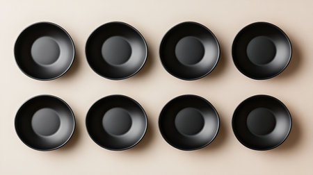 Discover an aerial view of eight minimalist black plates arranged symmetrically on a light background, showcasing clean lines and modern aesthetics.の素材