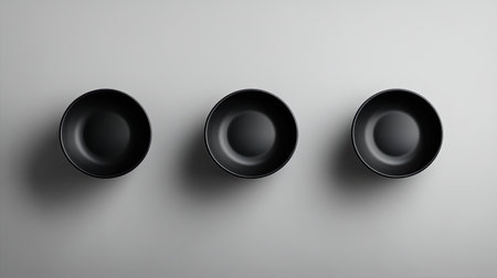 Three sleek black bowls are neatly arranged in a straight line on a soft grey background, emphasizing minimalism and elegance in design.の素材