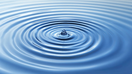 Close-up image depicting a droplet creating ripples on a calm water surface. The serene blue tones and circular patterns evoke tranquility and beauty, perfect for wellness themes.の素材