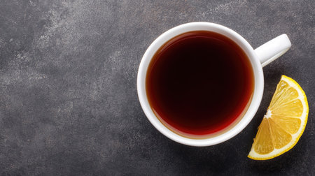 A top view of a hot cup of tea placed on a dark stone surface alongside a fresh lemon slice. Ideal for wellness and beverage themes, this visually appealing image evokes comfort and relaxation.の素材