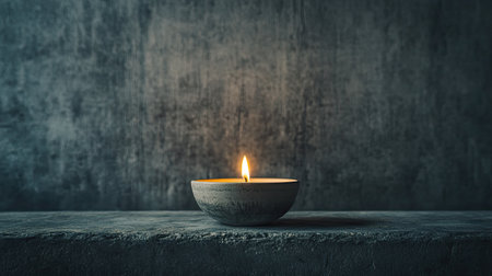 A serene image featuring a single candle placed in a bowl with a flickering flame, set against a dark textured background. Perfect for themes of tranquility and relaxation.の素材