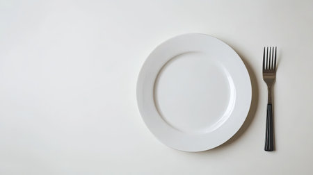 A minimalistic setup featuring an empty white plate and a fork on a light surface. Ideal for representing dining concepts, meal preparation, and culinary arts.の素材