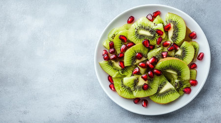 A vibrant arrangement of fresh kiwi slices topped with ruby red pomegranate seeds on a white plate, perfect for healthy desserts or snacking ideas.の素材